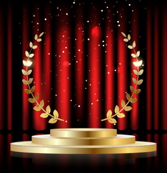 Golden laurel wreath over red round podium with steps in front of the curtains.